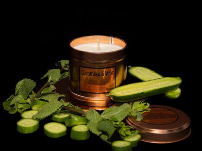 Irish Soy Wax Candle labeled 'Cucumber & Mint' surrounded by sliced cucumbers and mint leaves on a dark background. Copper Tin