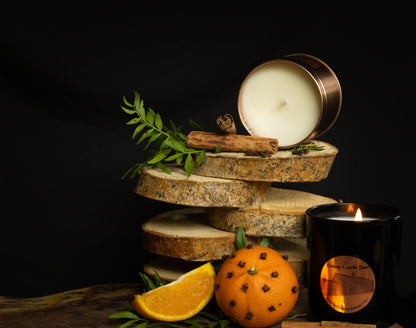 Irish Soy Wax Candle in a tin with a wooden coaster, orange slice, cinnamon stick, and clove studded clementine on a dark background.